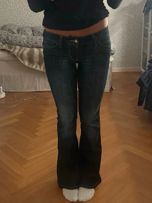 Mörkblå bootcut jeans lågmidjade - Säljer soprena mörkblå jeans med bootcut passform och låg midja. Klassisk femficksmodell med kontrastsömmar och guldfärgad knapp. Sitter tajt över låren och släpper ut nedtill för en snygg siluett. Perfekta till sneakers eller boots.