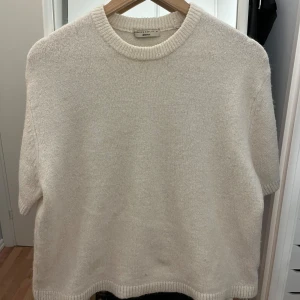 Vit stickad kortärmad tröja gina tricot - Säljer en varm vit, stickad tröja från gina tricot med rund hals och korta ärmar. Tröjan har en mjuk och lite loose passform, perfekt för lager på lager under vår och höst. Ribbad kant vid hals, ärmslut och nederkant för en clean look.