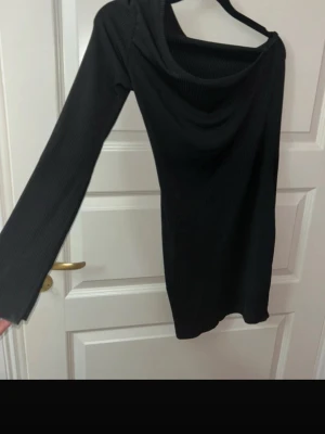 Svart ribbad klänning från SHEIN - Svart ribbad kortklänning från SHEIN i storlek S. Klänningen har lång ärm och en snygg, lite lösare halsringning. Tillverkad i mjukt och stretchigt material som sitter bekvämt på kroppen. Perfekt för dig som gillar enkel men stilren look.