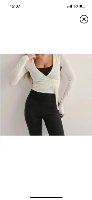 Vit omlottopp med knyt från Nelly - Säljer en vit omlottopp från Nelly i storlek S. Toppen har långa ärmar, v-ringad hals och snygg knytning i midjan. snygg till både träning och till ett par jeans!❤️