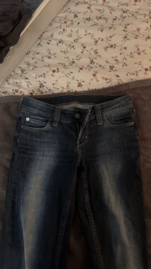 Cheap Monday Jeans Lågmidjade - Snygga mörkblå jeans från Cheapmonday med slitningar och ett unikt patch med döskalle på bakfickan. Klassisk femficksmodell, kontrastsömmar och normal passform. Perfekt för dig som vill sticka ut med detaljer och streetkänsla. Kommer ej till användning. De är i storlek 26/32 men har klippt bort lappen då den skavde. Kan gå ner i pris😊