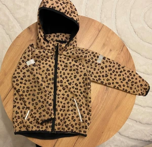 Jacka  - Snygg vindjacka från H&M med leopardmönster i beige och brunt. Jackan har huva, svarta detaljer, dragkedja framtill och två fickor med dragkedja. Perfekt för dig som gillar djurmönster och vill sticka ut lite extra.