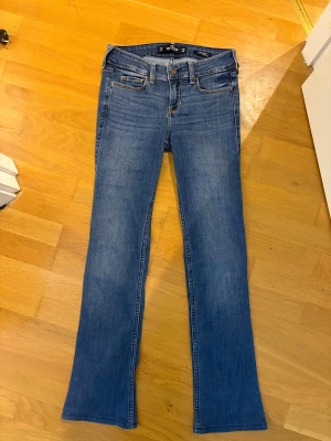 Blå bootcut jeans från Hollister W25 L32 - Snygga blå bootcut jeans från Hollister med klassisk stretch. Låg midja och femficksmodell, coola detaljer på bakfickorna och bruna sömmar. Köpta här på plick men säljer för att de tyvärr inte passade