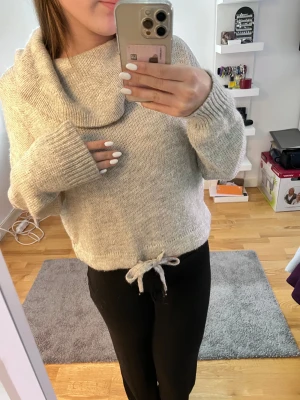Beige stickad tröja med krage från H&M - Supermysig beige stickad tröja från H&M i storlek S. Tröjan har en bred, nedvikt krage och långa ärmar med ribbade muddar. Nedtill finns en snygg knyt-detalj som ger extra stilpoäng. Perfekt för kyliga dagar och enkel att matcha med jeans eller leggings.