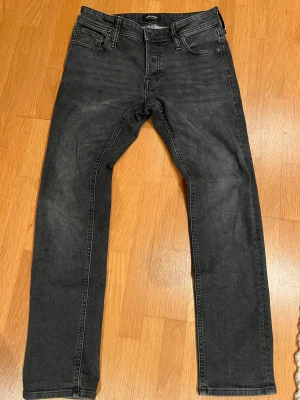 Svarta jeans från Jack & Jones - Snygga svarta jeans från Jack & Jones med klassisk femficksdesign och smal passform. Jeansen har en mörk tvätt och raka ben, perfekt för dig som gillar stilrena och enkla jeans. Materialet är mjukt och stretchigt denim för extra komfort.