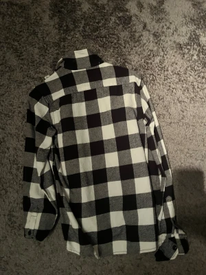 Svartvit rutig skjorta från Dickies - Snygg svartvit rutig skjorta från Dickies i storlek Small. Skjortan har klassisk krage, långa ärmar med manschett och knappar framtill. Perfekt för dig som gillar streetwear och vill ha en chill, loose passform. Materialet är mjukt och känns som bomull.