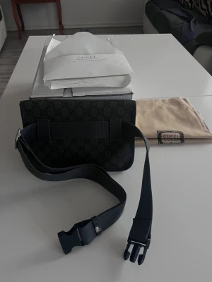 Svart axelväska från Gucci med GG-mönster - Snygg svart axelväska från Gucci med klassiskt GG-mönster över hela väskan. Väskan har en justerbar rem med spänne och silverfärgad GG-logga framtill. Materialet är en mix av skinn och syntet, perfekt för dig som gillar stilrena designer och exklusiva detaljer.