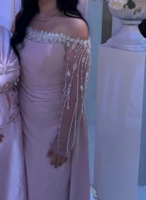 Ljusrosa långklänning  - Säljer en elegant ljusrosa långklänning med offshoulder och transparenta långärmar dekorerade med pärlor och glittriga detaljer. Klänningen har en vacker spetskant vid halsen och ett svepande släp. Perfekt för bal eller fest, riktigt princess vibes! Storlek är 42 men funkar för 40 också. Pris kan diskuteras 