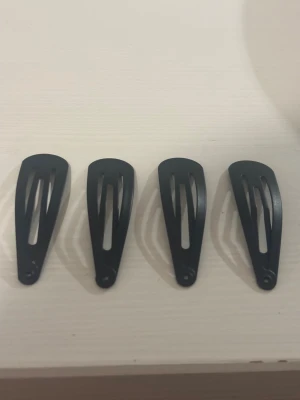 Svarta hårclips i metall, 4-pack - Fyra stilrena svarta hårclips i klassisk snap-modell. Perfekta för att hålla håret på plats och ge en clean look. Clipsen är av metall och har en enkel, avlång form som passar både till att styla luggen eller hålla undan hårslingor.pris kan diskuteras!💕