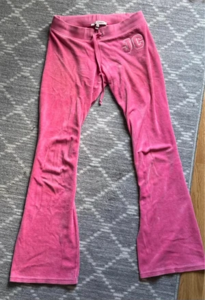 Rosa Juicy Couture mjukisbyxor XS - Säljer ett par ikoniska rosa mjukisbyxor från Juicy Couture i storlek XS. Byxorna har broderade JC-bokstäver på höften, snörning i midjan och är tillverkade i mjuk bomull och polyester. Modellen har bootcut och ger en chill vibe.