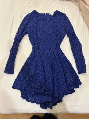 Blå spetsklänning från H&M - Snygg blå klänning från H&M med långärmade spetsdetaljer och rund hals. Klänningen har en figurnära passform upptill och ett utställd kjolparti, samt dragkedja i ryggen. Spetsen har ett blommigt mönster som ger en cool och romantisk vibe.