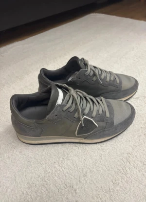 Grå Philippe Model sneakers strl 40 - Snygga grå sneakers från Philippe Model, tillverkade i Italien. Skorna har en mix av mocka och textil, med klassisk snörning och rund tå. Sidan pryds av den ikoniska skölden och sulan är platt med svart mönster undertill. Perfekt för dig som gillar stilrena och exklusiva sneakers. Perfekt nu inför vintern till dig som inte vill bli blöt om fötterna när snön kommer. Box ingår.