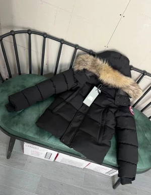 Svart Canada Goose dunjacka med päls - Säljer en svart dunjacka från Canada Goose med fluffig päls på huvan. Jackan har en klassisk puffer-look, långärmade ärmar och både dragkedja och knappar framtill. Märkets ikoniska patch sitter på ärmen. Perfekt för kalla vinterdagar.