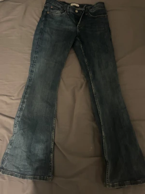 Blå bootcut jeans från Perfect Jeans - Säljer ett par blå bootcut jeans från Perfect Jeans i klassisk denim. Jeansen har fyra fickor, dragkedja och knapp framtill samt snyggt utsvängda ben. Perfekt för dig som gillar en retroinspirerad look och vill ha ett par jeans med lite extra attityd.