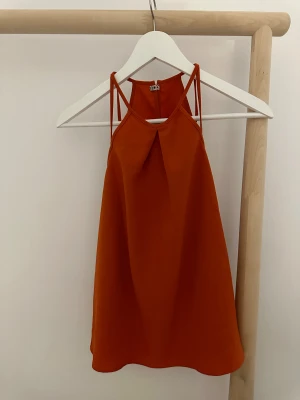 Orange linnetopp från H&M strl 36 - Säljer en snygg orange linnetopp från H&M i storlek 36. Toppen har smala axelband och en detalj med veck framtill. Materialet är mjukt och lätt polyester. Stängs med en liten hake i nacken och har en stilren, loose passform.