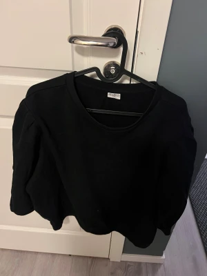 Svart tröja från & Other Stories - Svart tröja från & Other Stories med rund hals och puffade axlar. Tröjan har lång ärm och är gjord i mjuk bomull, perfekt för en chill och stilren look. Passar dig som gillar enkel men snygg design.