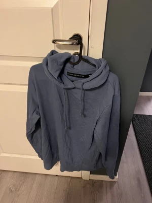 Blå hoodie från The Black Label - Säljer en stilren blå hoodie från The Black Label Collection. Tröjan har huva med snörning och långa ärmar, perfekt för en chill och avslappnad look. Mjuk och skön, passar till allt. Snygg basic som funkar året runt.