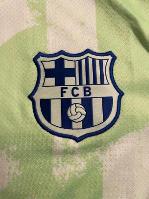Barcelona Dri-Fit fotbollströja Nike M - Fräsch Barcelona fotbollströja från Nike i ljusgrön och vit färg med tryckt Spotify-logga och FCB-emblem på bröstet. Kortärmad modell i Dri-Fit material som andas, perfekt för träning eller match. Snyggt mönster och broderad Nike-logga i blått och rött.