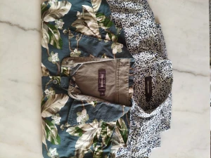 Två mönstrade skjortor från Dressmann - Säljer två kortärmade skjortor från Dressmann i storlek XL. Ena skjortan har ett blommigt mönster i grönt, beige och vitt på blå botten, medan den andra har ett prickigt mönster i svart och vitt. Båda har klassisk krage och knappar framtill. Perfekt för dig som gillar att sticka ut med mönster!Skjortorna är som nya.