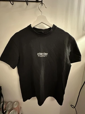 Svart t-shirt Crime Time från Smog XS - Svart t-shirt från Smog i relaxed fit med tryck 'crime time' och flera coola vita grafiska texter och motiv på ryggen, bland annat en drake och en fågel. Rund hals och korta ärmar. Materialet är mjuk bomull, perfekt för dig som gillar streetwear.