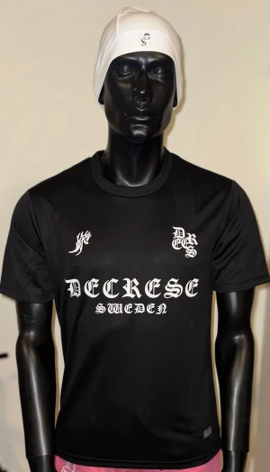 Decrese Sweden T-shirt – SvartSvart T-shirt  - Decrese Sweden T-shirt – Svart Svart T-shirt med vit Decrese Sweden-print i sportig matchtröjestil med streetwear-känsla. Lätt och bekväm passform, perfekt för vardag, gym och modern streetstyle. Extra snygg ihop med Decrese-mössan.