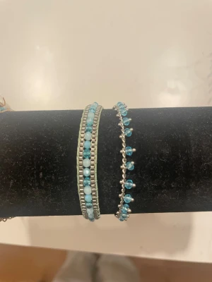 Två blå pärlarmband i silverfärg - Säljer två snygga armband med blå pärlor. Det ena har dubbla rader med små blå och vita pärlor infattade i silverfärgad kedja, det andra är tunnare med blå pärlor på rad och silverdetaljer. Perfekt för att ge din stil lite färg.
