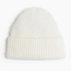 Vit ribbstickad mössa - Mysig vit mössa i ribbstickad design med uppvikt kant. Perfekt för kalla dagar och enkel att matcha med alla outfits. Tillverkad i ett mjukt och fluffigt material som håller dig varm hela vintern.