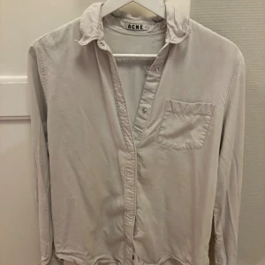 Acne skjorta - Säljer denna sjukt snygga acne skjorta i storlek M. Den är i riktigt bra skick och knappt använd. Den är i ljusgrå/beige färg.