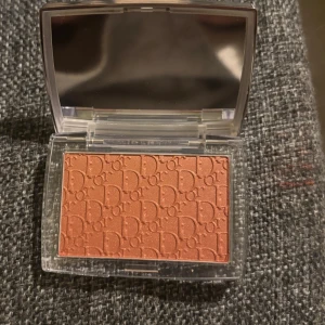 Dior persikofärgad rouge - Rouge från Dior i en snygg persikoton med lätt skimmer. Kommer i en elegant genomskinlig dosa med spegel och har Dior-loggan präglad i pudret. Perfekt för att ge kinderna en fräsch och glowig look.
