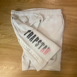 Trapstar vita shorts med tryck - Vita Trapstar shorts i storlek M med två framfickor och en bakficka med dragkedja med text tryck och snörning köpt på trapstar london hemsida 