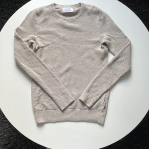 Beige stickad tröja från Strömberg - Snygg beige stickad tröja från Strömberg i storlek S. Tillverkad av ekologisk bomull och återvunnen polyester. Tröjan har rund hals, ribbade muddar och långärmad passform. Perfekt för dig som gillar stilrena och enkla plagg.