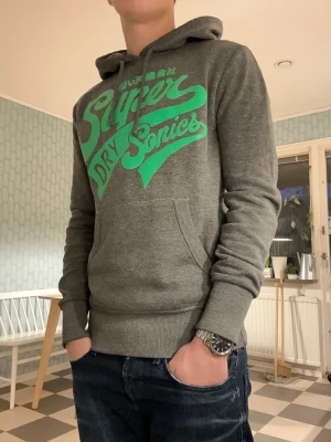 Superdry Sonics hoodie - En snygg superdry sonics hoodie i färg green/grey🤩! Storlek S, är 176cm lång på bilderna. Inga tecken på slitage och är i princip ny från fabriken😮‍💨Kontakta mig vid frågor samt prisförslag😄! Mvh