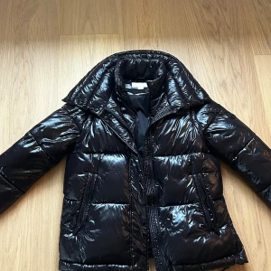Svart pufferjacka Michael Kors S - Svart glansig pufferjacka från Michael Kors med hög krage och två sidofickor med dragkedja. Jackan har ett Michael Kors märke på ärmen. Den är köpt 2024 och är knappt använd. Skriv om det önskas mer bilder!🥰