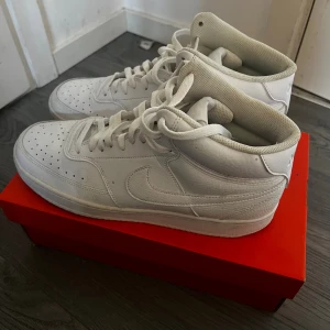 Nike Air Force 1 Mid helvita sneakers - Säljer ett par klassiska Nike Air Force 1 Mid i helvitt skinn. Skorna har perforerad tå, snörning och den ikoniska swoosh-loggan på sidorna, använd ett par gånger men säljs eftersom den inte kommer till användning längre, pris går att diskutera 