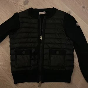 Moncler Cardigan - Säljer en snygg svart cardigan från Moncler. Jag köpte jackan i juli och den är fortfarande i nyskick. Jackan passar mig som brukar ha xs/s. Den är i storlek 1 (som motsvarar S) Det går att scanna qr koden i jackan. Skriv för fler bilder eller frågor🥰
