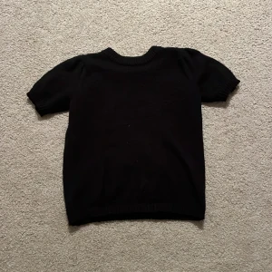 Svart stickad tröja med puffärm - Svart stickad tröja med korta puffärmar och rundad ribbad halsringning. Mjuk och skön känsla, perfekt för dig som gillar enkel stil med en twist. Passar dig som vill ha något klassiskt men ändå lite extra. Snygg att matcha med jeans eller kjol. Tröjan har några noppror men inget man tänker på! 