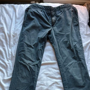 Grå slim fit chinos från J.Lindeberg - Snygga grå chinos från J.Lindeberg i slim fit-modell. Byxorna har en rak och smal passform med klassisk design, tillverkade i mjukt bomullsmaterial. Perfekta för dig som gillar stilrena och moderna byxor med en clean look.