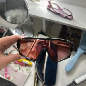 Helt nya oakleys  - Säljer ett par svarta sportglasögon från oakley med bred, rödtonad lins och cool, futuristisk design. Glasögonen har en robust ram i syntetmaterial och passar perfekt för dig som gillar att sticka ut när du tränar eller cyklar.