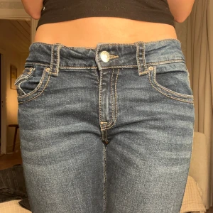 Blå bootcut jeans med hög midja - Snygga blå jeans med bootcut passform och medel midja. Klassisk femficksdesign, kontrastsömmar och knappstängning fram. Jeansen har en lätt tvättad look och är tillverkade i jeansmaterial med stretch för skön passform. Sprättade längst ner