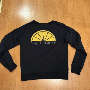 Mörkblå  sweatshirt från Acqua Limone - Mörkblå sweatshirt från Acqua Limone i storlek M. Tröjan har ett stort gult citrontryck och logga på ryggen samt diskret logga framtill