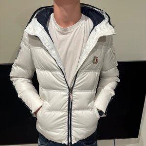   Dolomite jacka - Säljer en snygg vit pufferjacka från Dolomite med broderad logga och text på ryggen. Jackan har huva, dragkedja framtill och flera innerfickor med coola detaljer. Insidan är marinblå och jackan har en modern, normal passform. Perfekt för kalla dagar! 