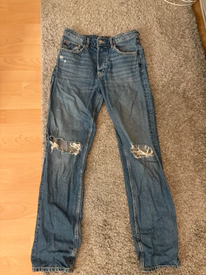 Jeans - Blåa jeans med hål vid knäna och även ett litet i bakfickan, välanvända st 36