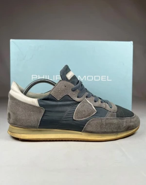 Philippe model gråa  - Snygga sneakers från Philippe Model i gråblått med detaljer i mocka och textil. Skorna har klassisk snörning, vit häl. Ikonisk sköld på sidan och rund tå ger en stilren vibe. Perfekta för dig som gillar en clean men sportig look. Passar även storlek 44. Riktigt fint skick. 