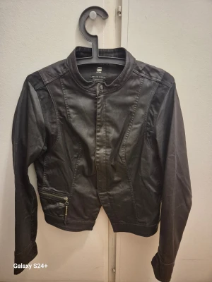 Svart bomberjacka från G-Star RAW - Snygg svart bomberjacka från G-Star RAW med coola detaljer som dragkedja och RAW-logga på fickan. Jackan har en modern, kortare passform och är tillverkad i ett syntetmaterial med matt finish. Perfekt för dig som gillar streetstyle och vill ha en jacka med attityd.