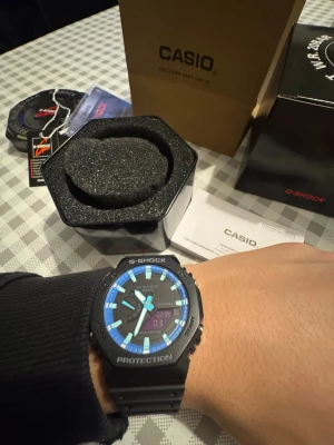 Casio G-Shock GA-2100 klocka svart/blå - Casio G-Shock GA-2100 med svart resinarmband och boett, digital och analog urtavla med blå detaljer. Klockan har octagonal form, Carbon Core Guard, vattentät till 200m och levereras med originalbox, taggar och manual.