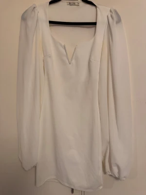 Vit långärmad klänning från Nelly XS - Vit klänning från NLY One i storlek XS. Modellen har långa puffärmar och en djup v-ringning med unik detalj framtill. Klänningen är kort och har en stilren, minimalistisk look.