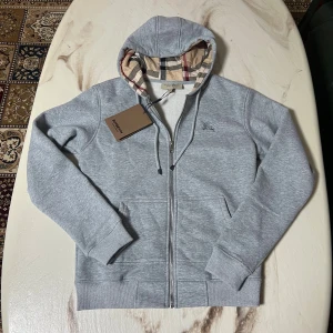 Grå Burberry hoodie med dragkedja - Snygg grå hoodie från Burberry. Helt ny och använd bara en gång. Den passsade inte mig då den var för liten för mig. Den är storlek S och är felfri!
