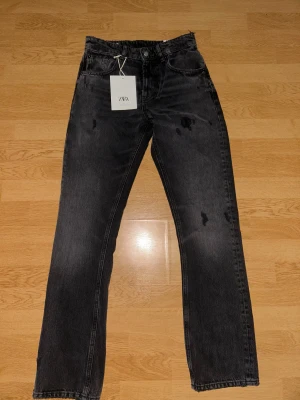 Svarta straight jeans från Zara, strl 36 - Säljer ett par svarta jeans från Zara i storlek 36. Modellen har midja i midwaist, raka ben och relaxed fit. Jeansen är i klassisk svart tvättad denim med fem fickor och knappgylf. Perfekta för en clean och avslappnad look.