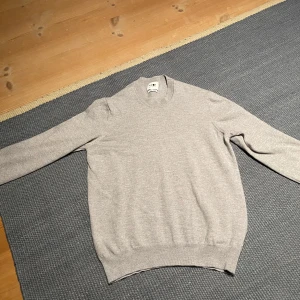Ljusgrå stickad tröja från NN07 - Snygg ljusgrå stickad tröja från NN07 med rund hals och ribbade muddar. Tillverkad av italienskt garn för en mjuk och skön känsla. Perfekt för dig som gillar stilrena och enkla plagg. Passar dig som vill ha en klassisk look. Det finns ett väldigt litet hål under armen som inte syns vid användning. Hör av dig vid frågor eller funderingar!