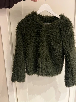 Grön ”pälsjacka” från Jacqueline de Yong - Säljer en fluffig och cool mörkgrön ”pälsjacka” från Jacqueline de Yong i storlek XS. Jackan är tillverkad i syntetmaterial med mjuk, lurvig yta. Perfekt för dig som vill sticka ut med en trendig look. Fint skick!